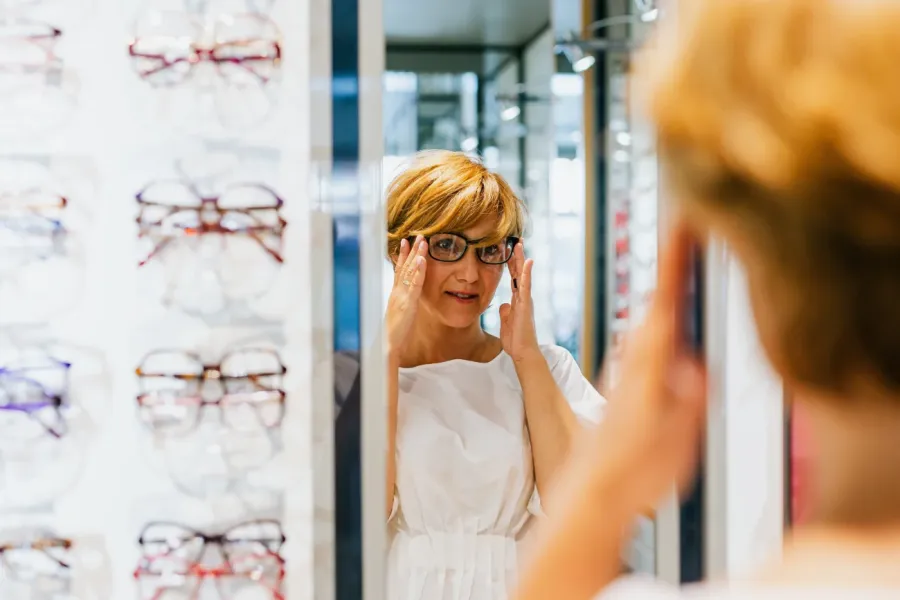 woman in an optical store tries on glasses in front of a mirror